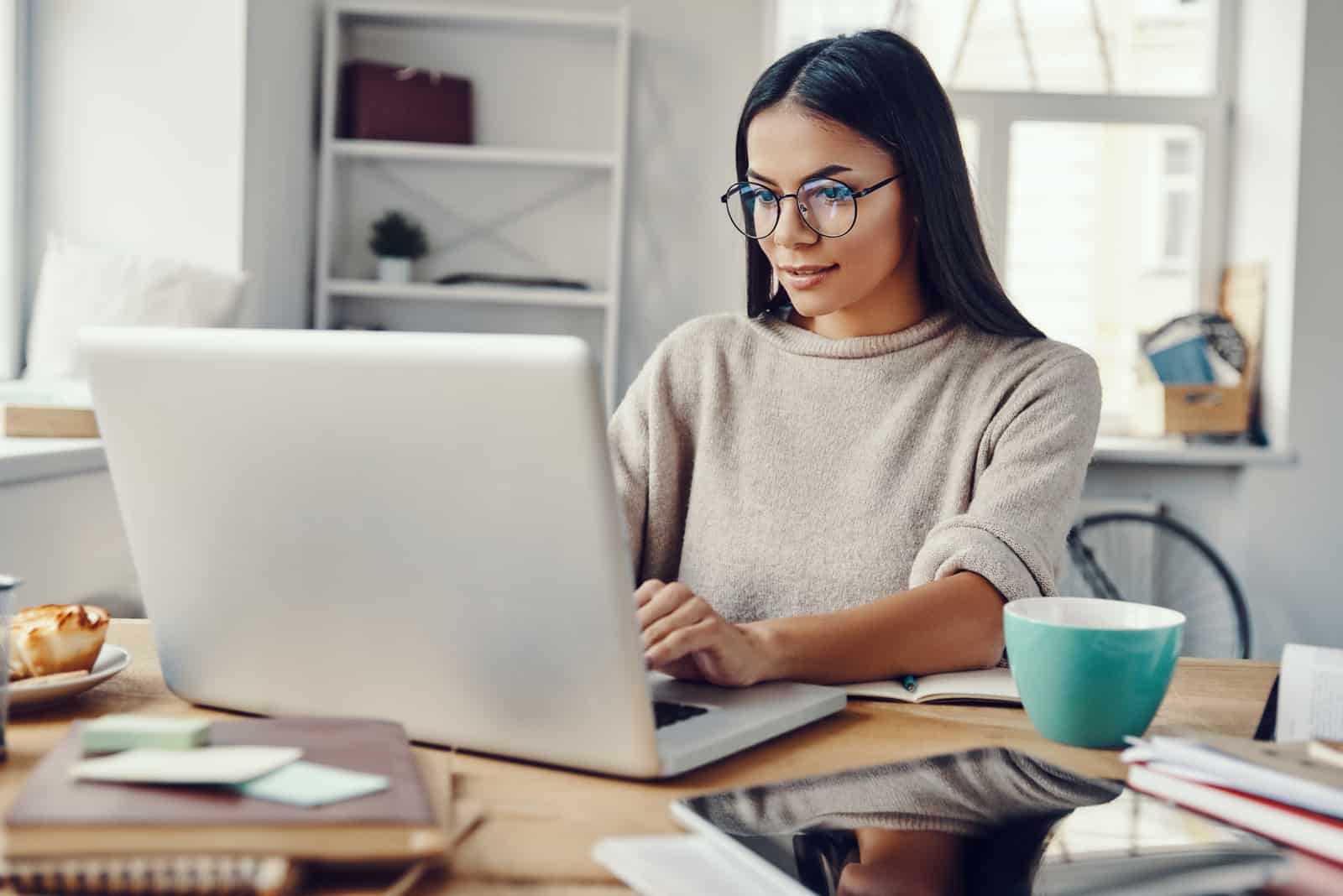 una mujer con el pelo largo y negro es sentado y trabajando detrás de una computadora portátil