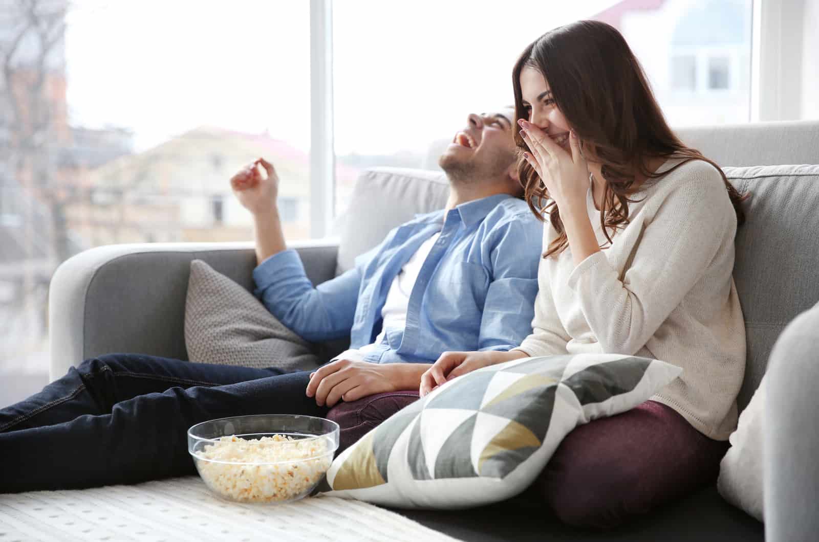 pareja riéndose comiendo palomitas de maíz en el sofá