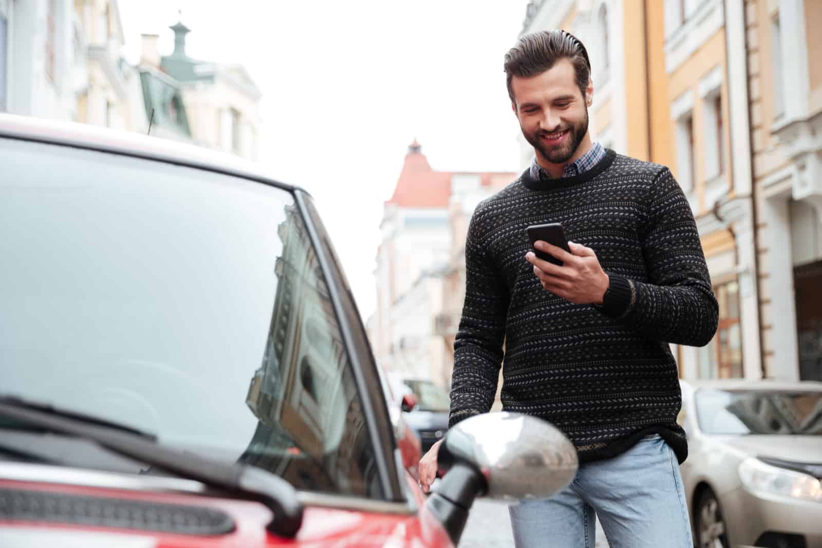 Un joven sonriente parado al lado de un auto y presionando un botón de teléfono