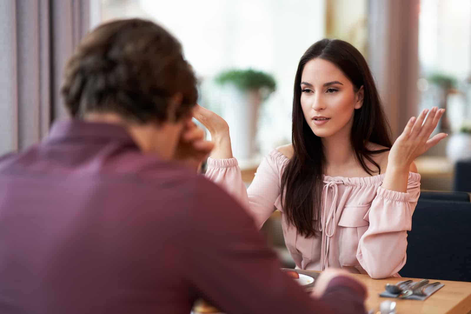 un hombre y una mujer discuten en un café mientras están sentados cara a cara