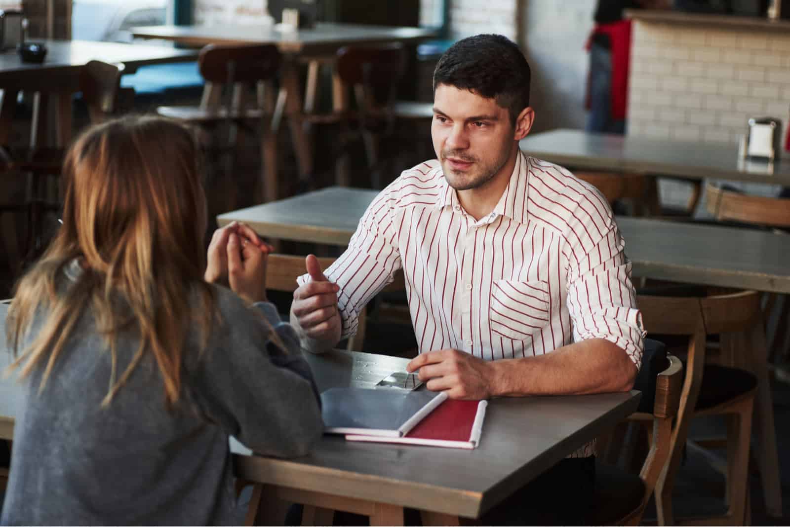 un hombre y una mujer están hablando en un café mientras están sentados cara a cara