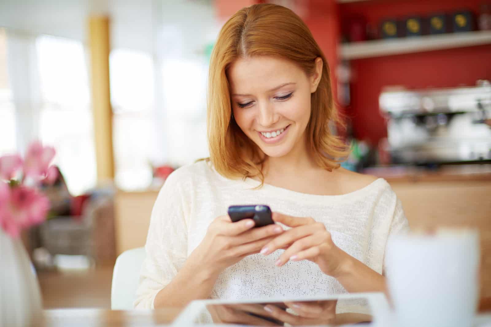 una mujer sonriente está sentada y sosteniendo un teléfono en la mano