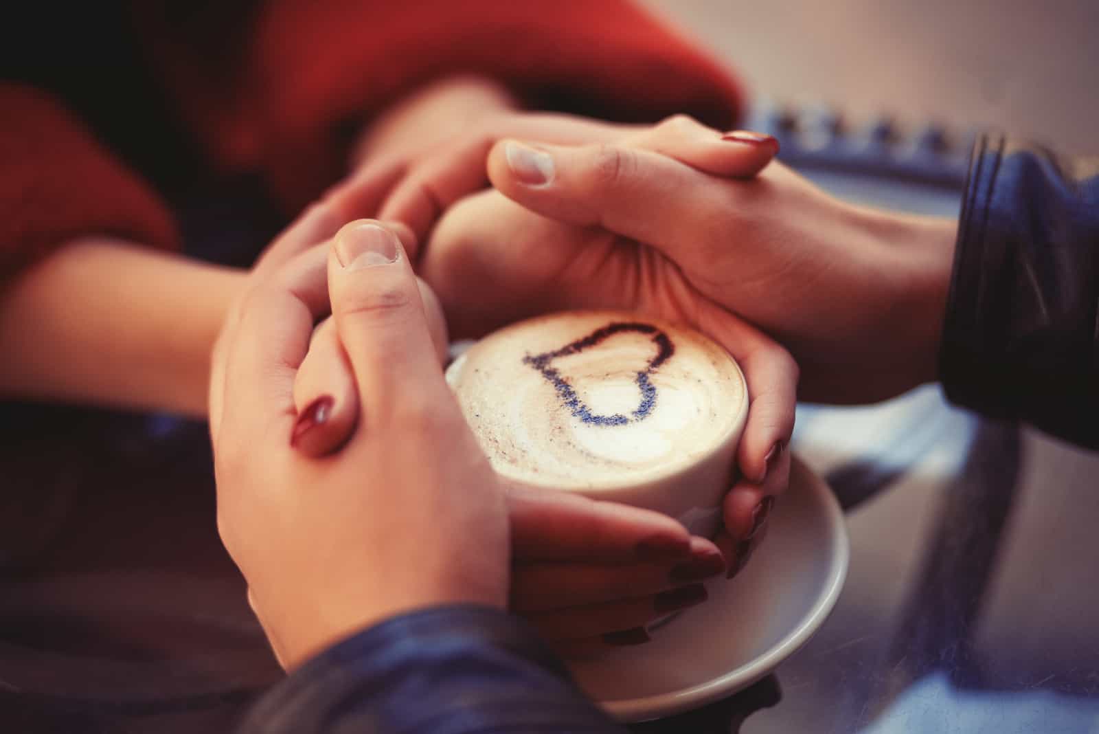 pareja tomados de la mano con una taza de café entre