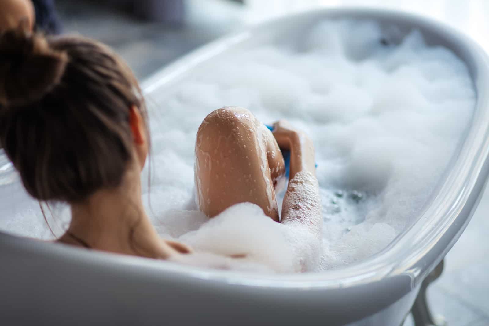mujer masajeando sus piernas con una esponja en la bañera