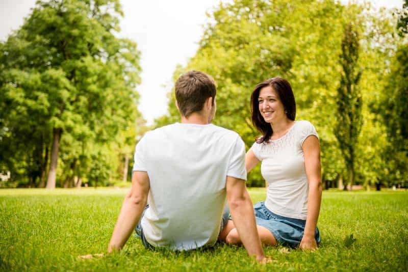 Una joven pareja feliz charlando al aire libre, sentada en el césped