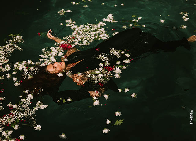 Foto de una mujer flotando en el agua con pétalos de rosa.