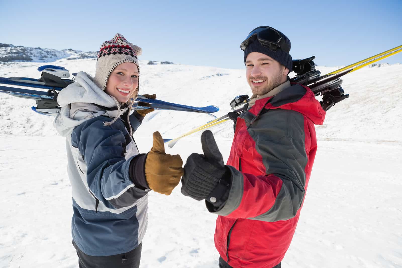 Vista trasera retrato de pareja sonriente con tablas de esquí gesticulando sobre el paisaje cubierto de nieve