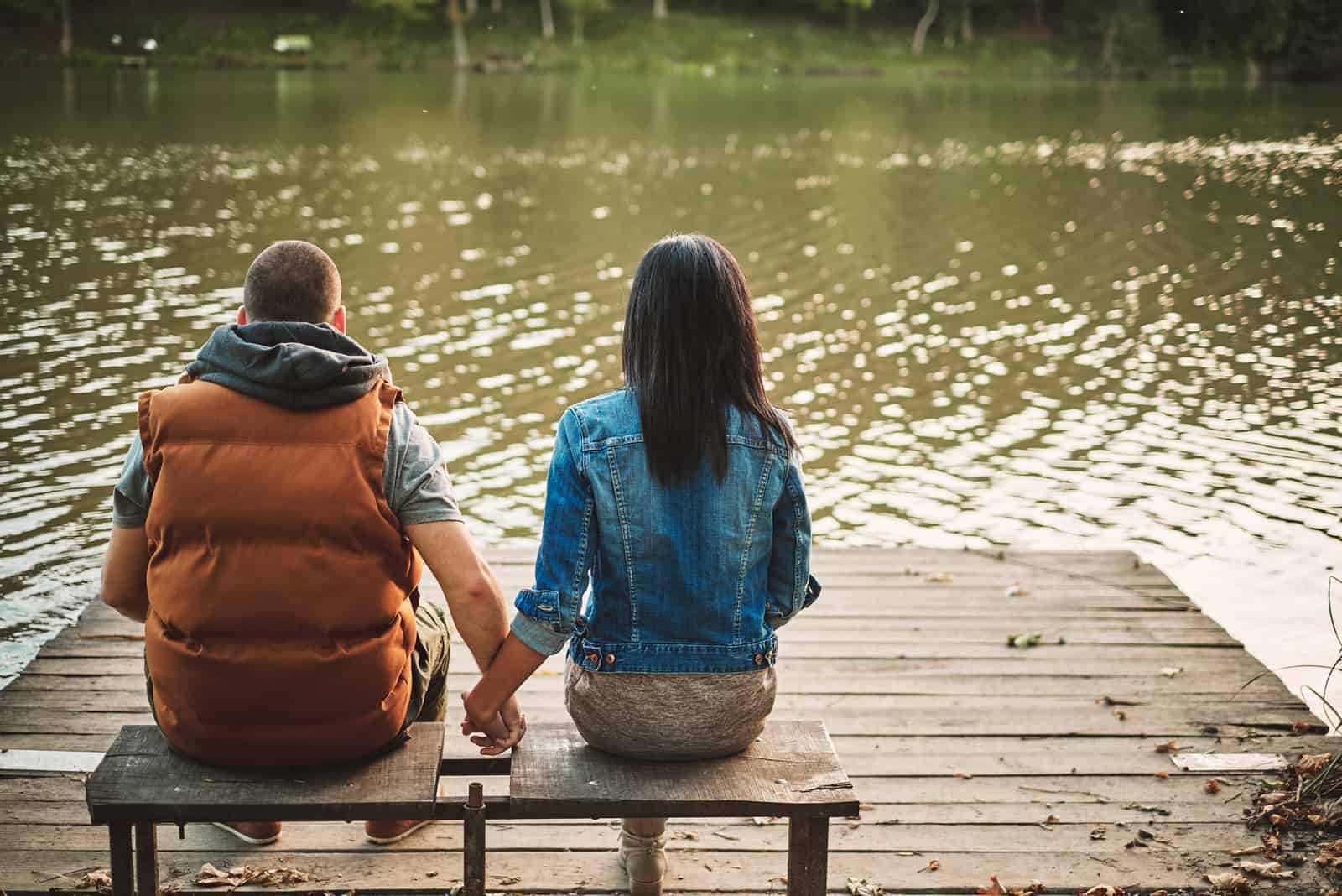 pareja sentada junto al lago tomados de la mano