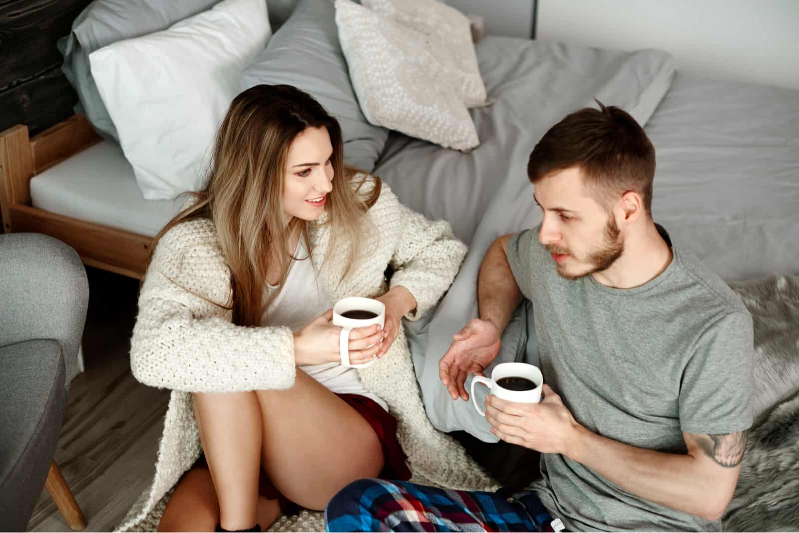 pareja hablando sentada en el suelo con una taza de café en la mano