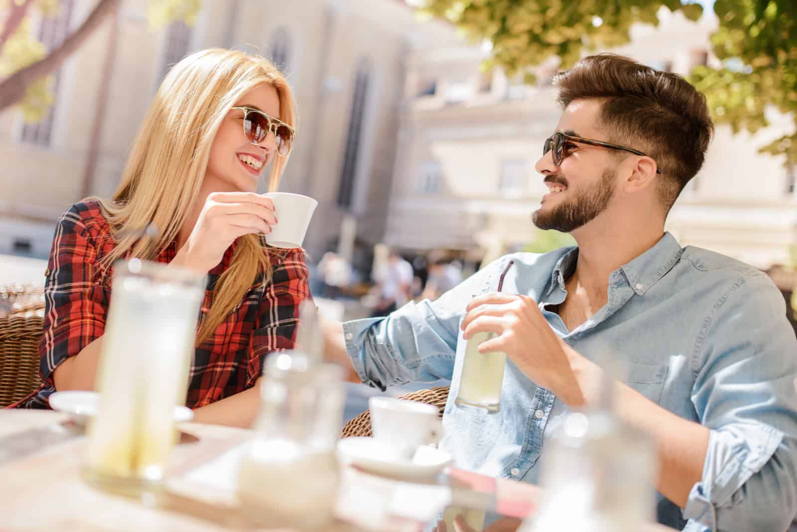 un hombre y una mujer están sentados afuera tomando café