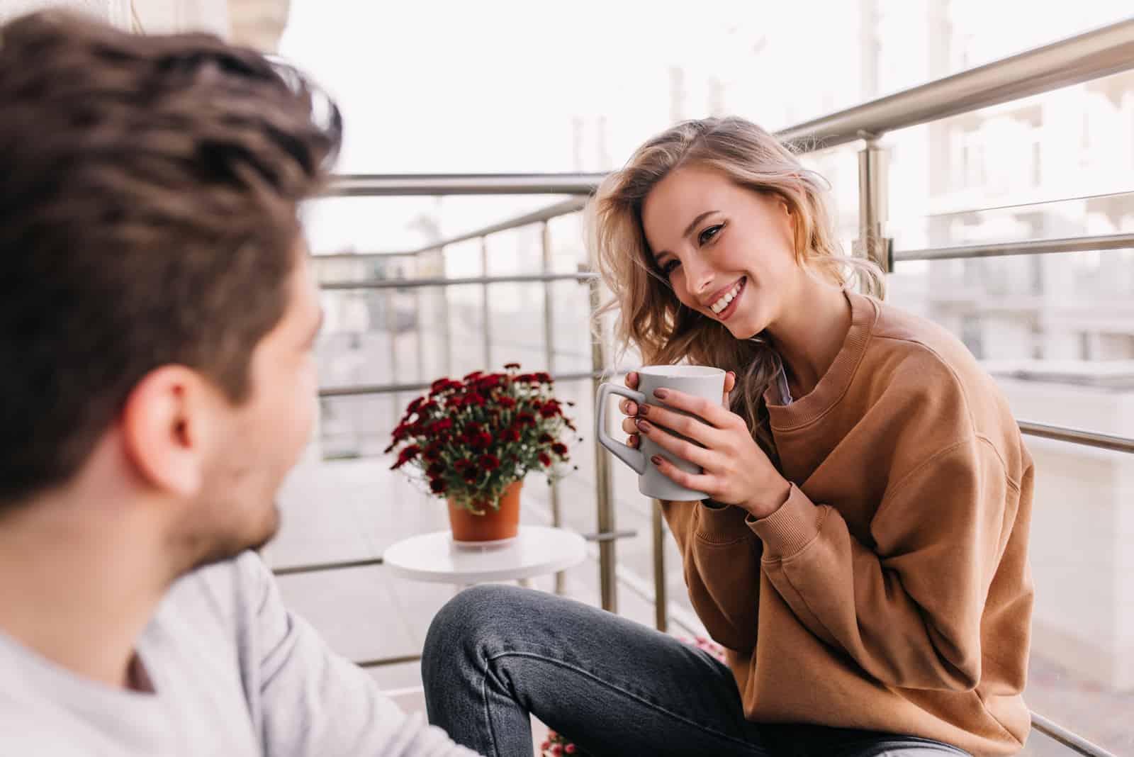un hombre y una mujer sentados en el balcón tomando café hablando