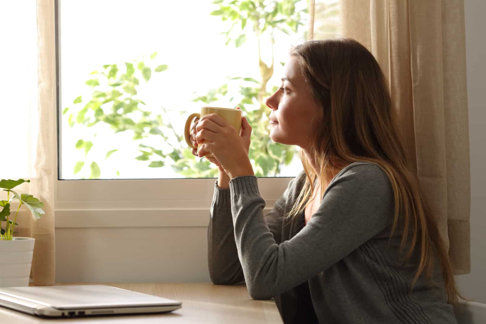 Una mujer imaginaria sentada junto a la ventana con una taza en la mano.