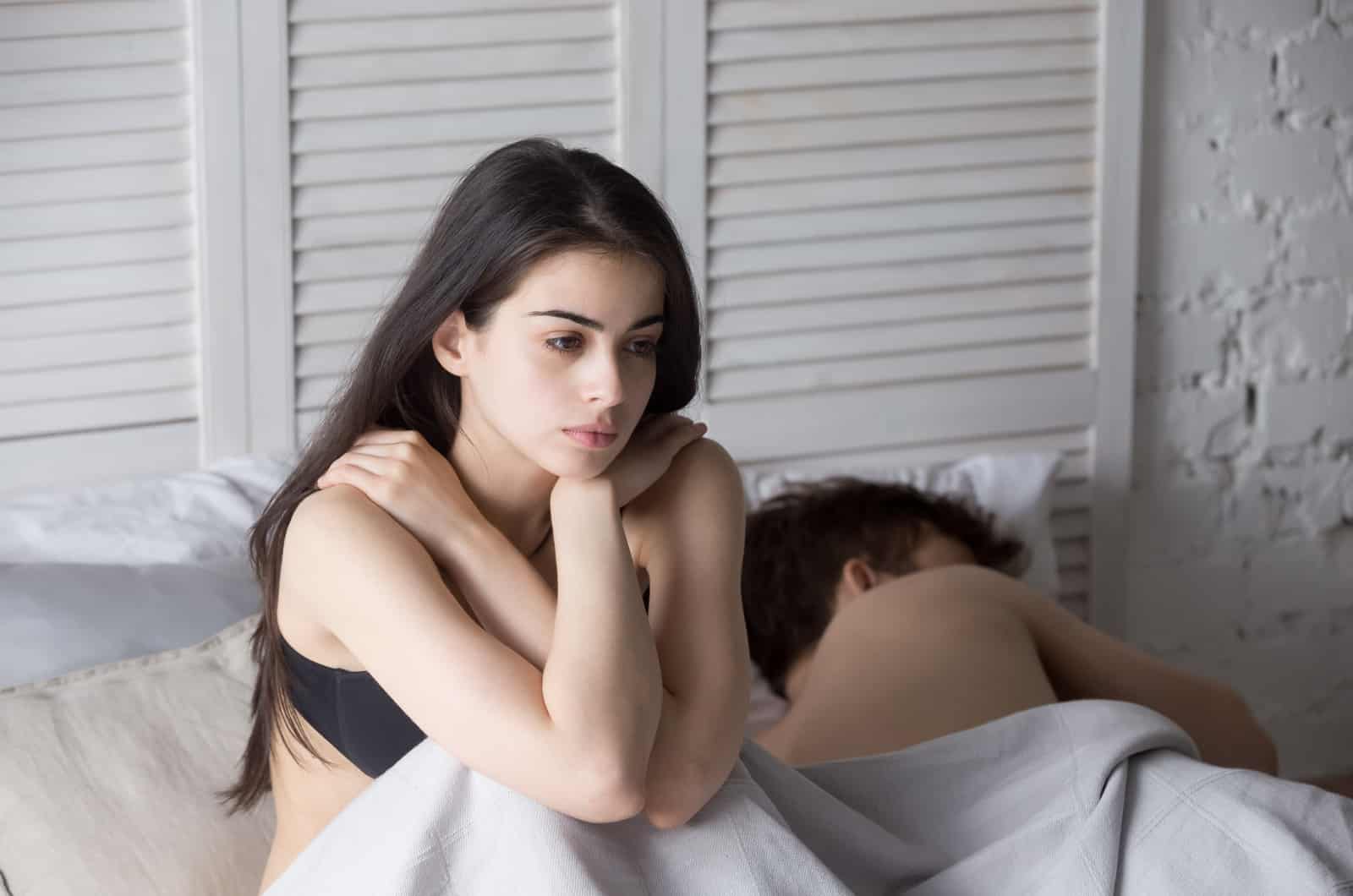 mujer sentada en la cama mientras su novio duerme